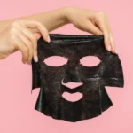 Two hands holding a black Korean charcoal face mask for skin beauty